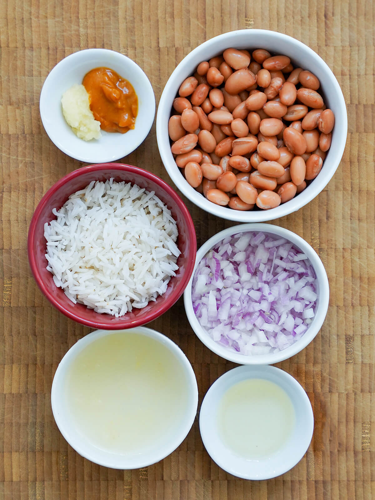 bowls of beans, cooked rice, chopped onion, stock, oil and garlic and chili pastes.