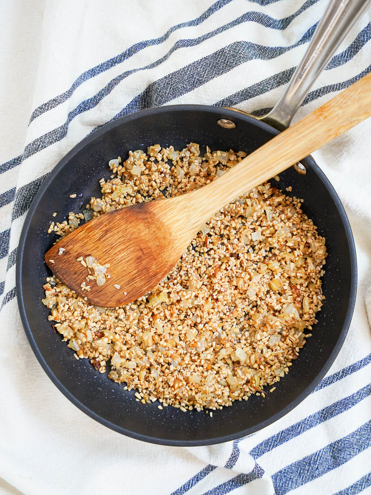 overhead view of skillet of skirlie oatmeal stuffing with wooden spoon on top.