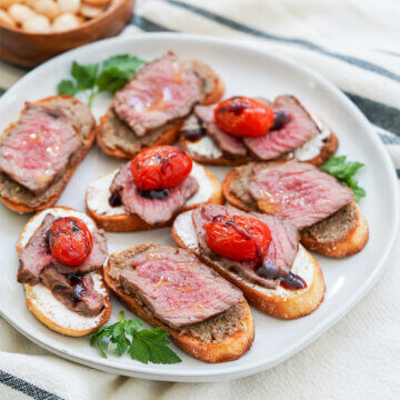 plate of steak crostini, some with pate under steak and others with goat cheese under and tomato on top.