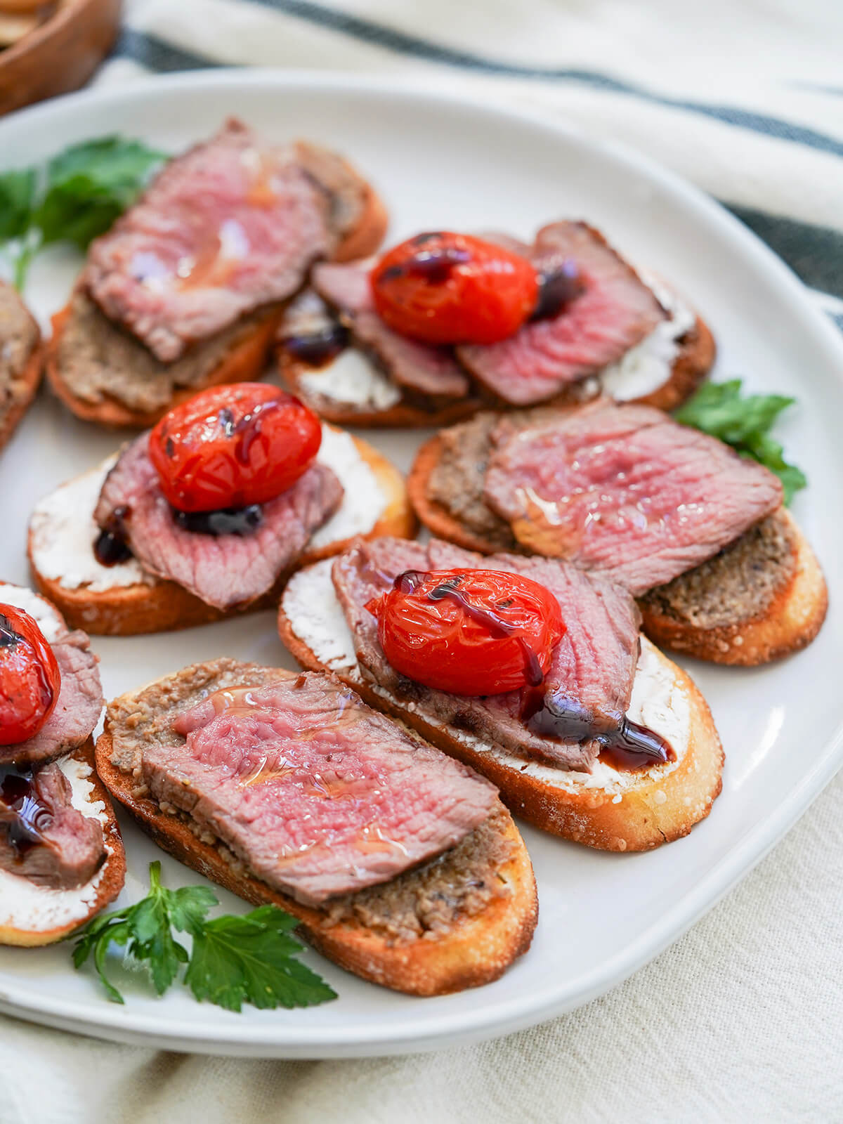 part view of plate of steak crostini, some with pate under steak and others with goat cheese under and tomato on top.