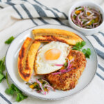 plate of tacu tacu, topped with egg, plantain on side, with small dish of salsa criolla behind
