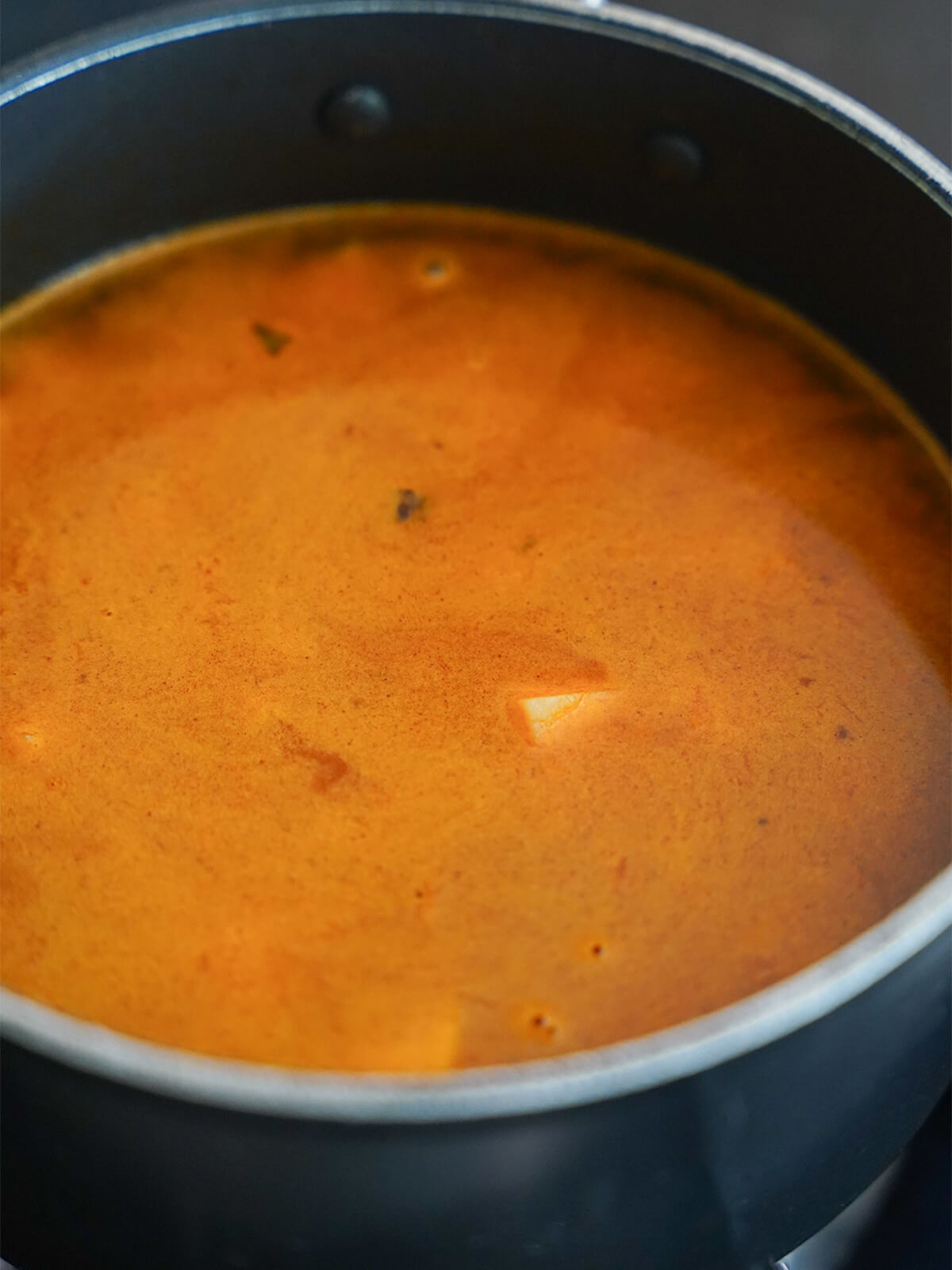liquid in pot colored from spices with a small edge of a potato chunk sticking out.