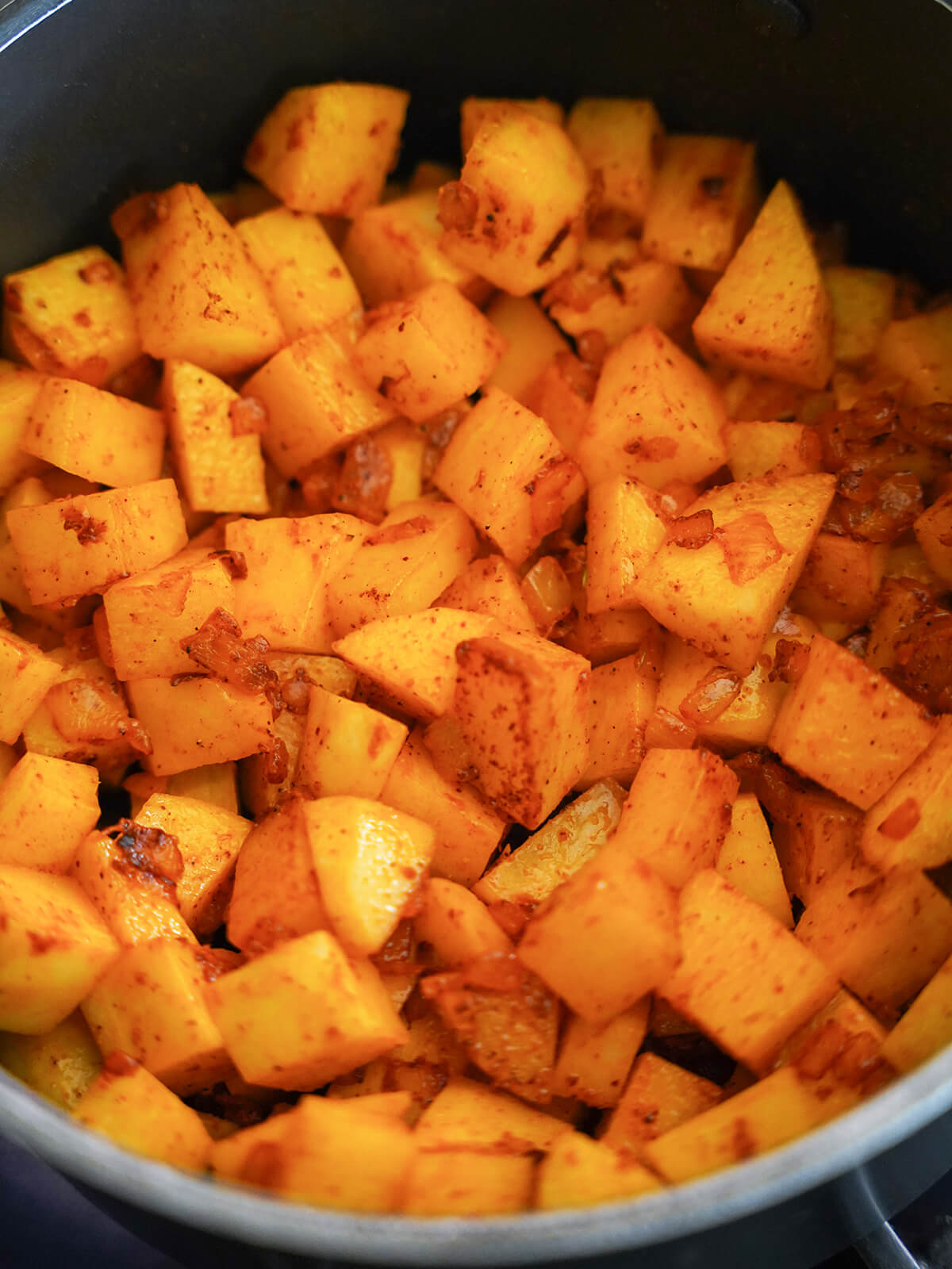 chunks of potato with onion and spices mixed through, colored red-orange from achiote.