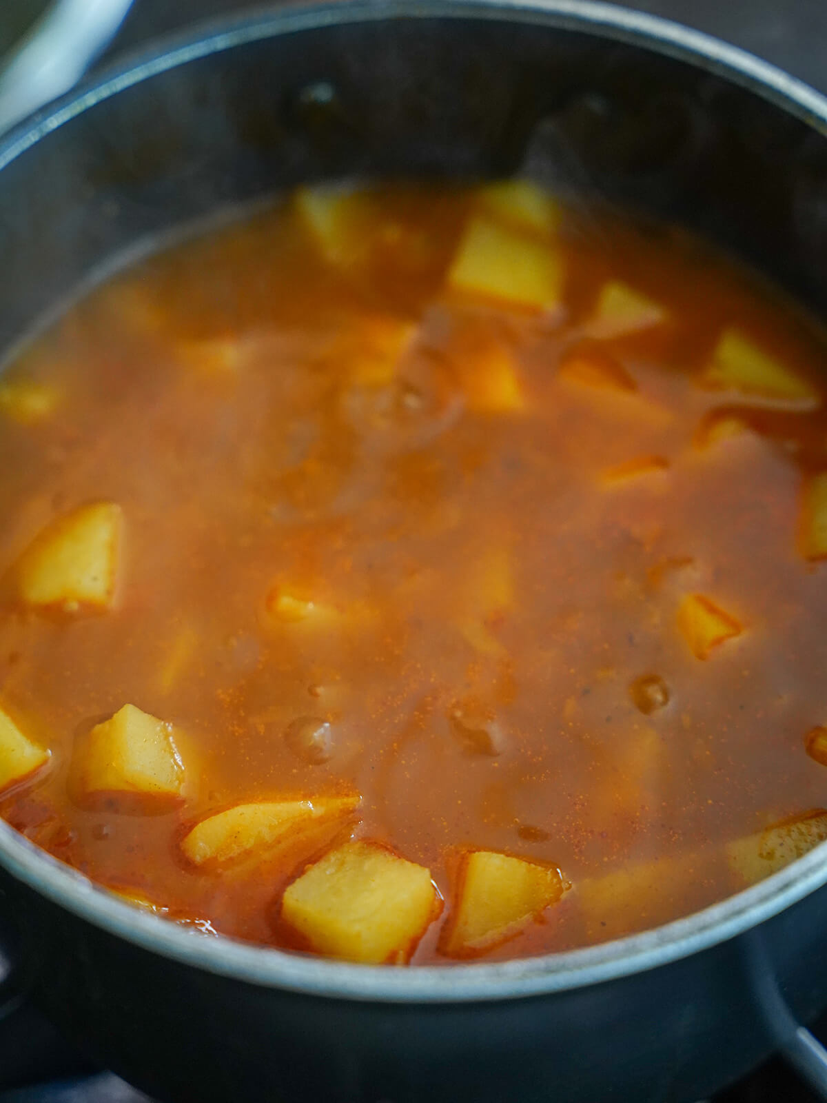 pot of unblended soup with red color to base and showing chunks of potato in mixture.