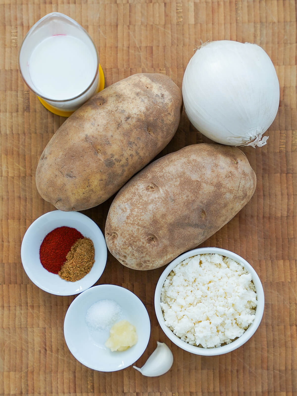 potatoes, onion, dish with crumbled cheese, measure of milk, small dishes with spices and garlic.