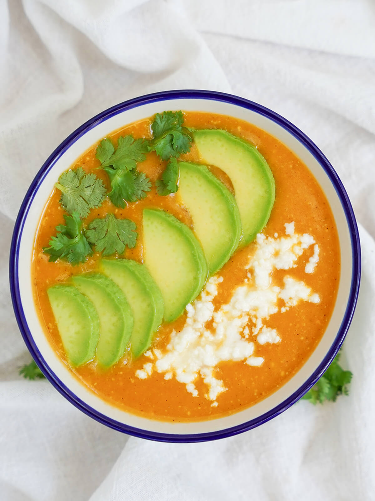 overhead view of bowl of locro de papa Ecuadorean potato soup topped with avocado slices, cheese and cilantro leaves.