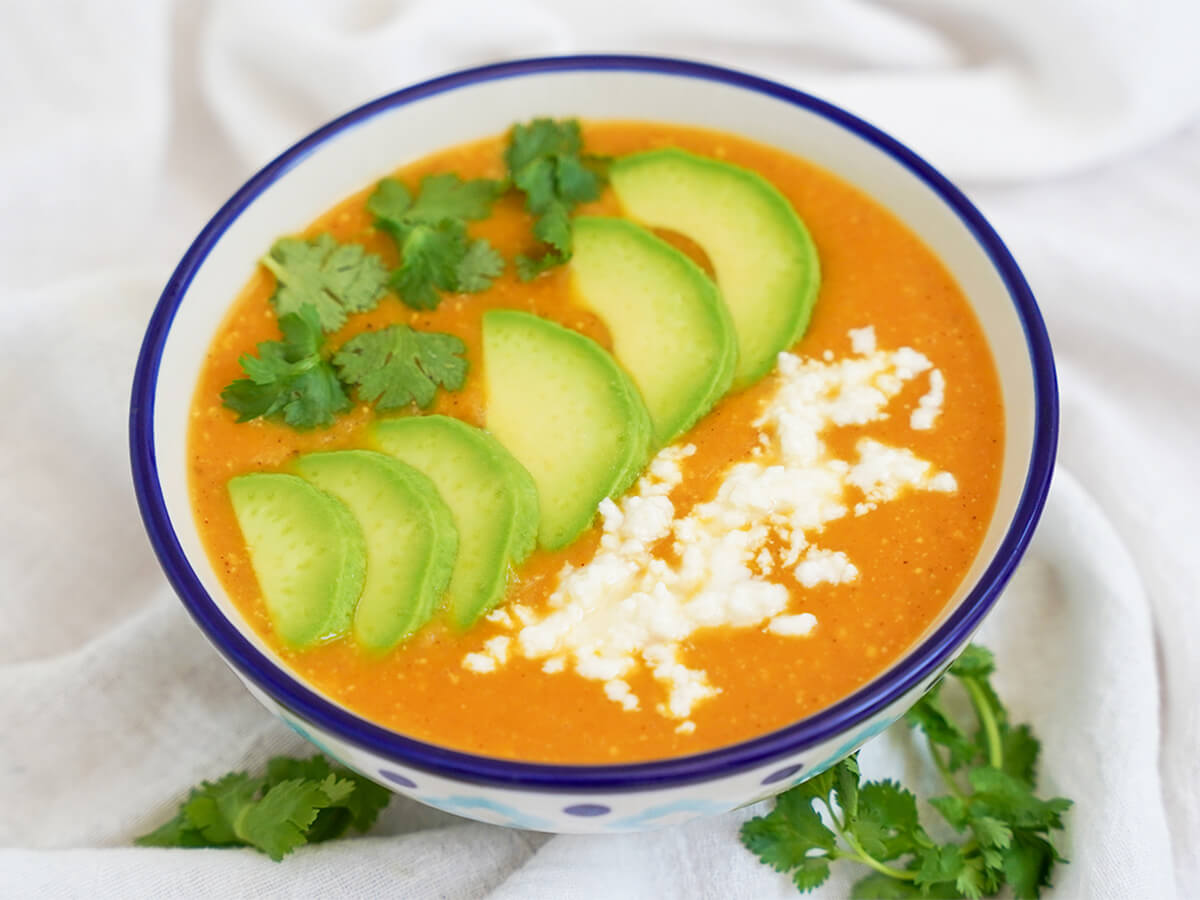 side view of bowl of locro de papa, Ecuadorean potato soup, topped with cilantro, avocado slices and crumbled cheese.