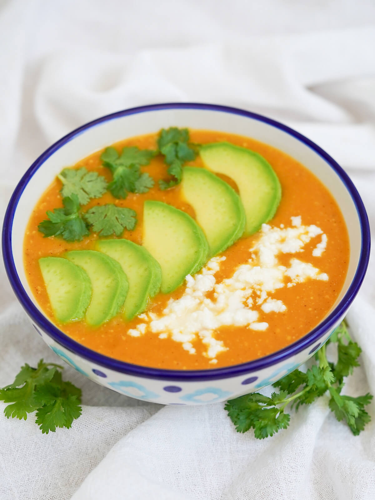side view of bowl of locro de papa, Ecuadorean potato soup, with cilantro under bowl and cilantro, cheese and avocado garnishes on top of soup.