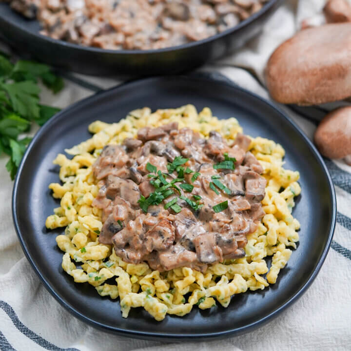 plate of mushroom stroganoff over spaetzle with part view of skillet behind with more sauce.