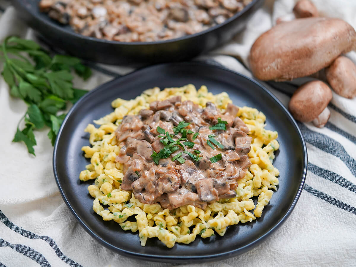 mushroom stroganoff served over spaetzle plate of mushroom stroganoff served over spaetzle with some mushrooms and parsley behind plate.