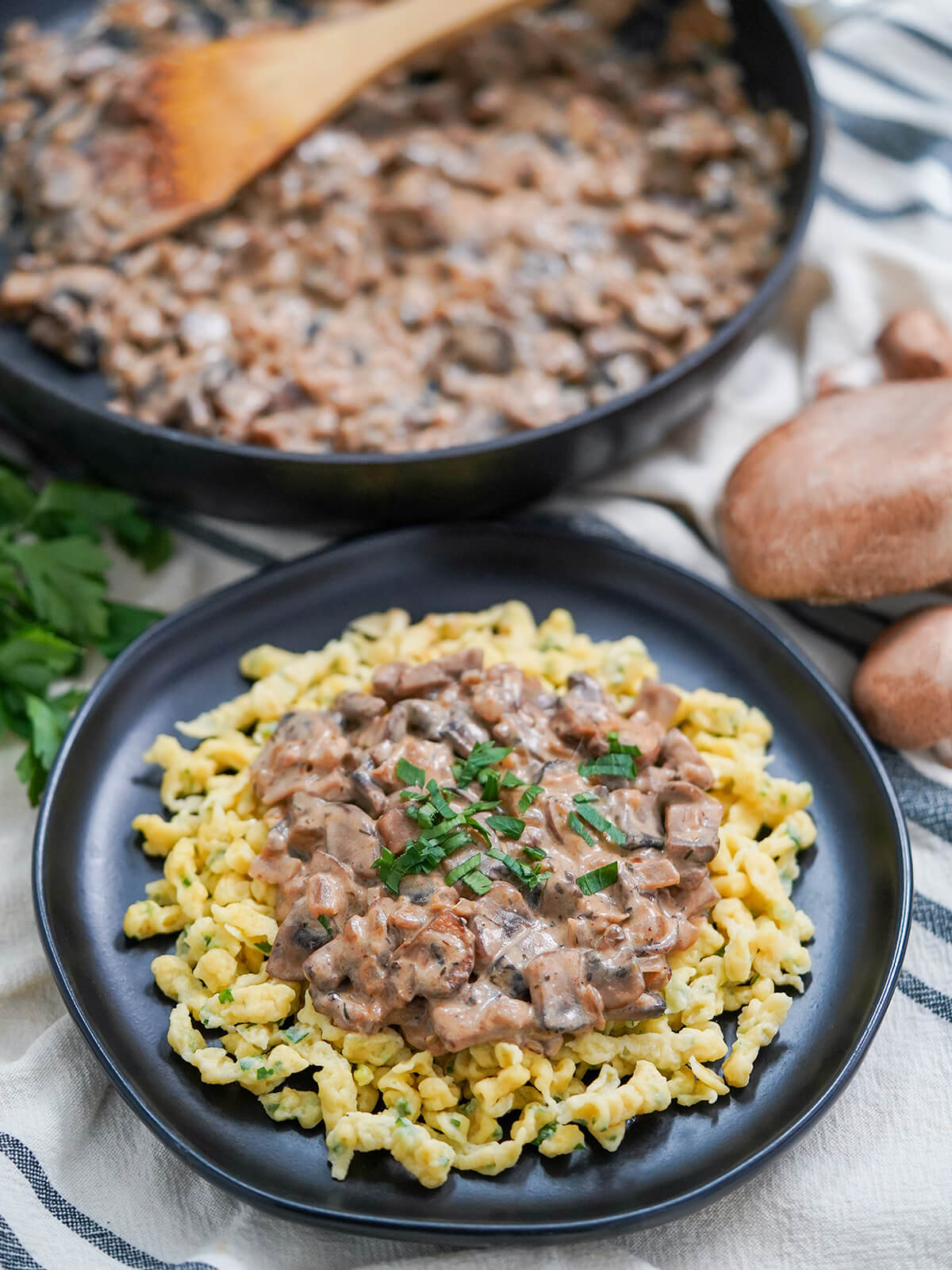 This mushroom stroganoff is quick and easy to make, with fantastic flavors and comfort factor. A great vegetarian main that's hearty and flavorful enough you won't miss the meat. mushroom stroganoff over spaetzle on black plate with skillet with more behind.
