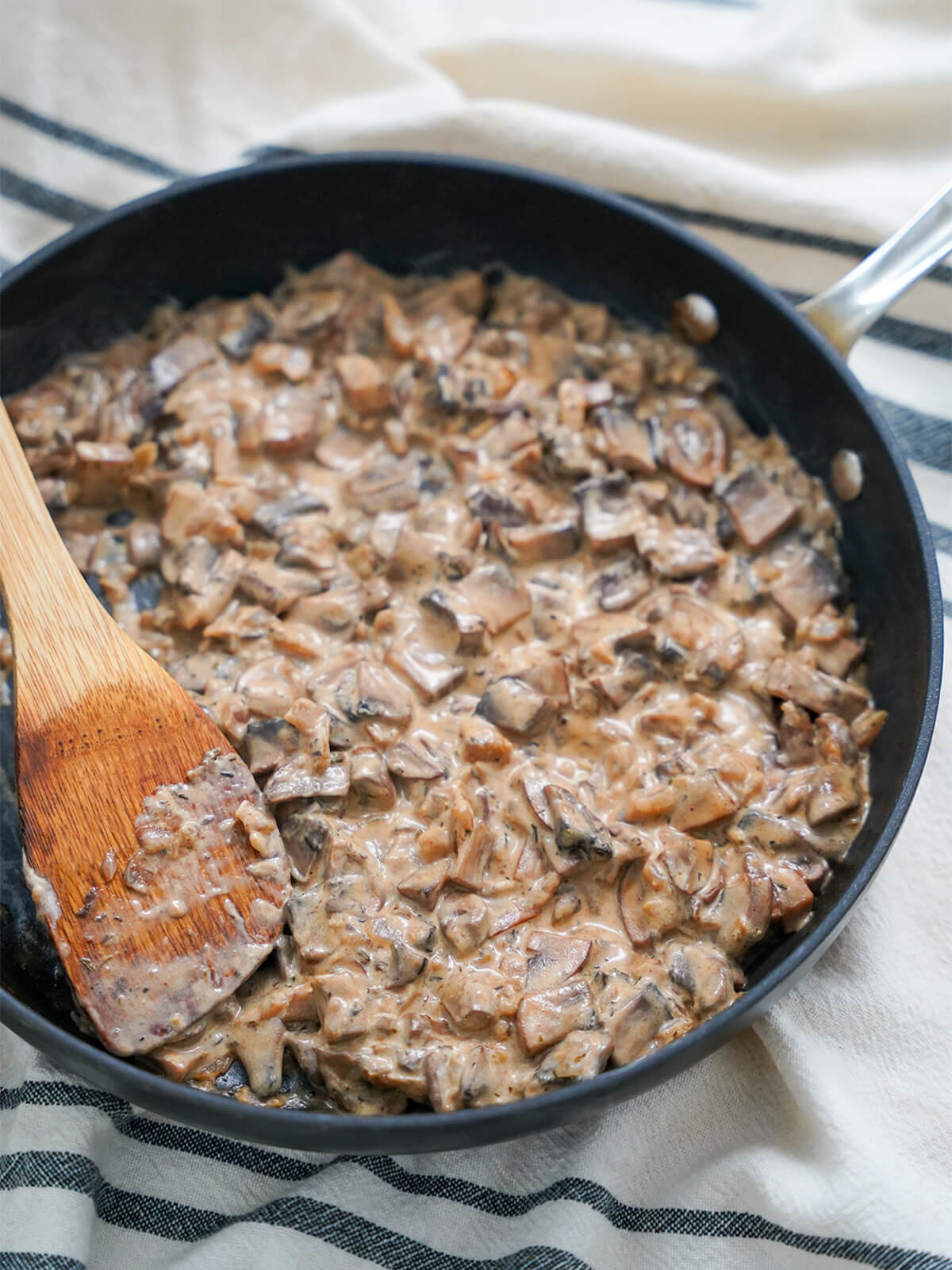 skillet of creamy mushroom stroganoff. skillet of mushroom stroganoff showing creamy sauce with wooden spatula to side.