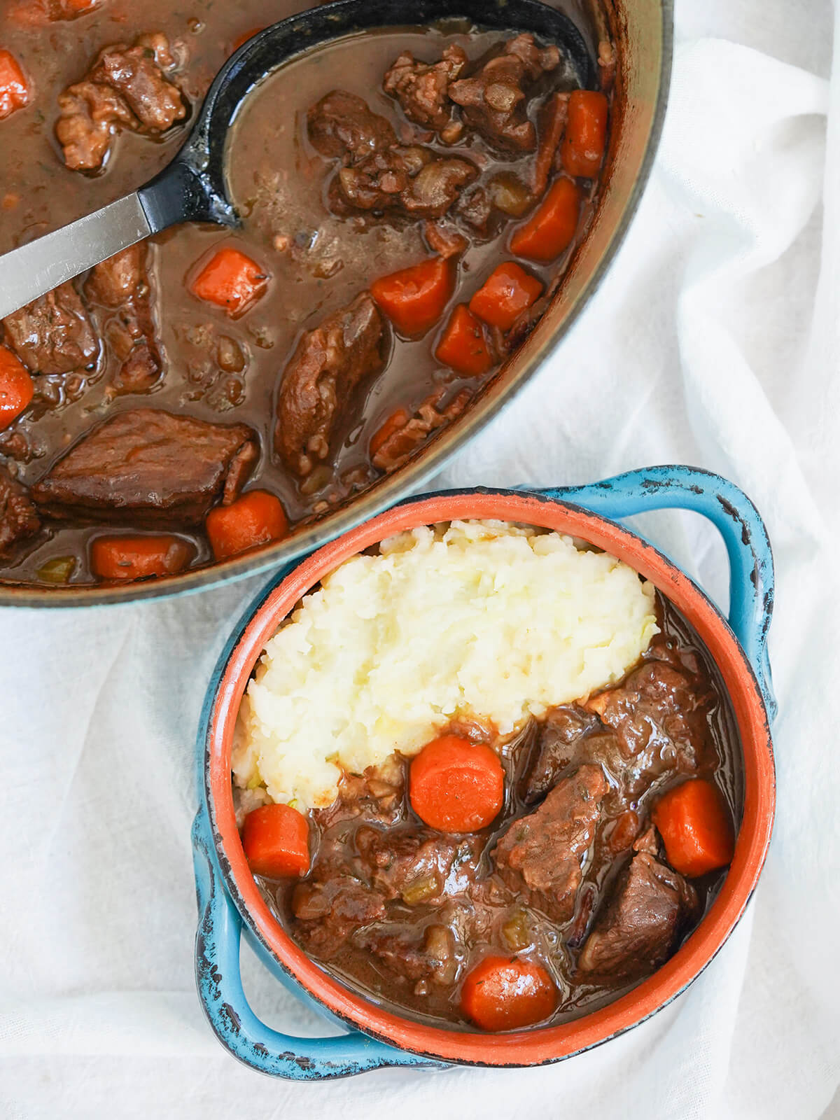 overhead view of bowl of Guinness beef stew and pot of stew with spoon resting in it.