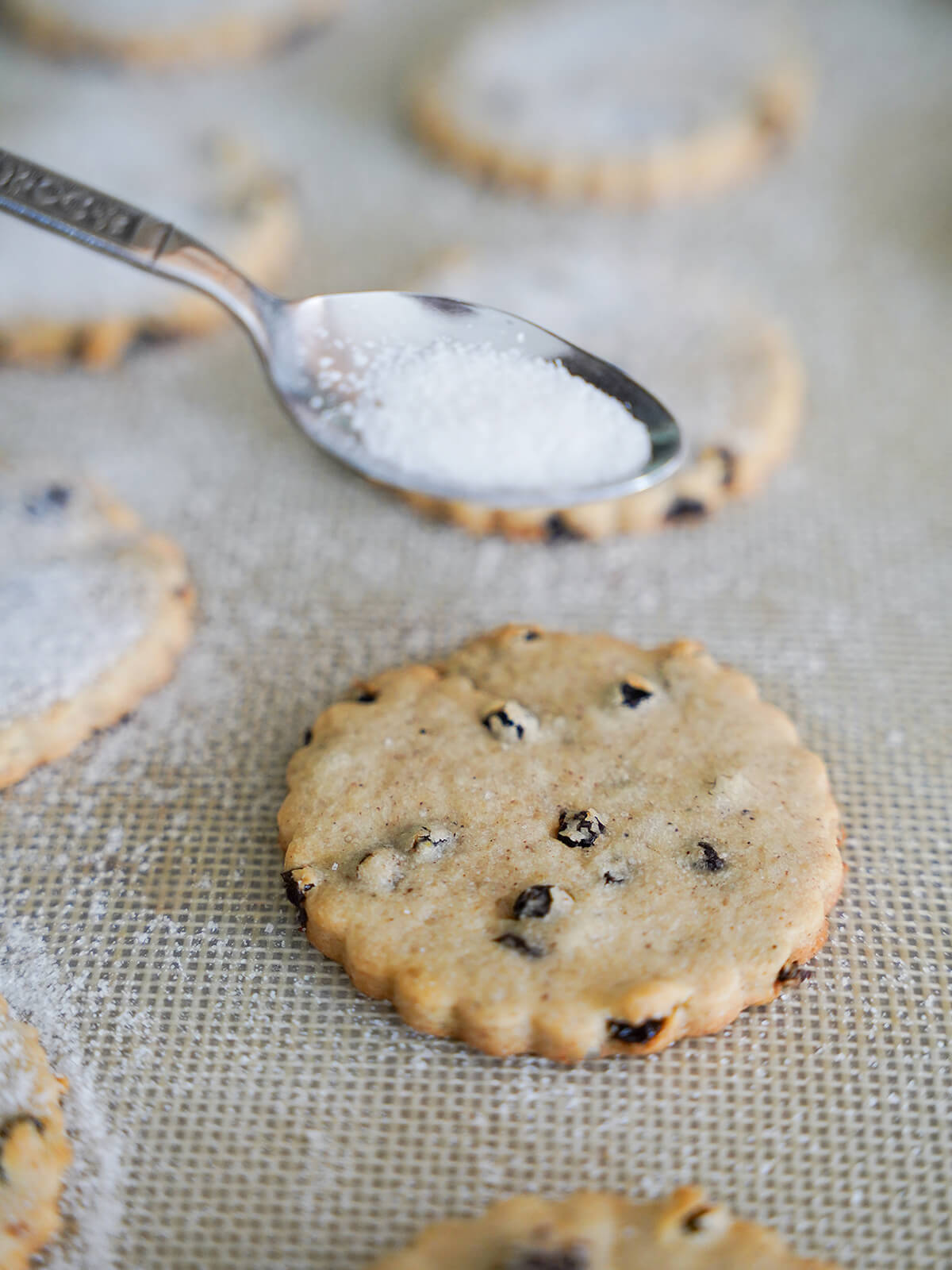 sprinkling sugar over biscuit/cookie that is just out oven on lined baking sheet.