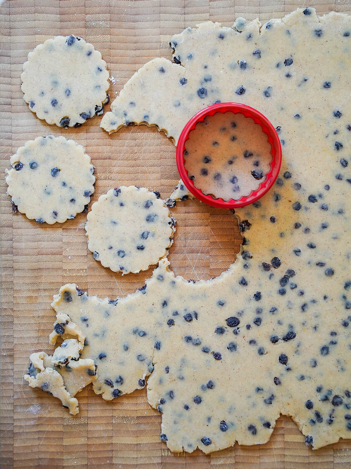 cutting out fluted circles of currant-speckled dough on wooden board.
