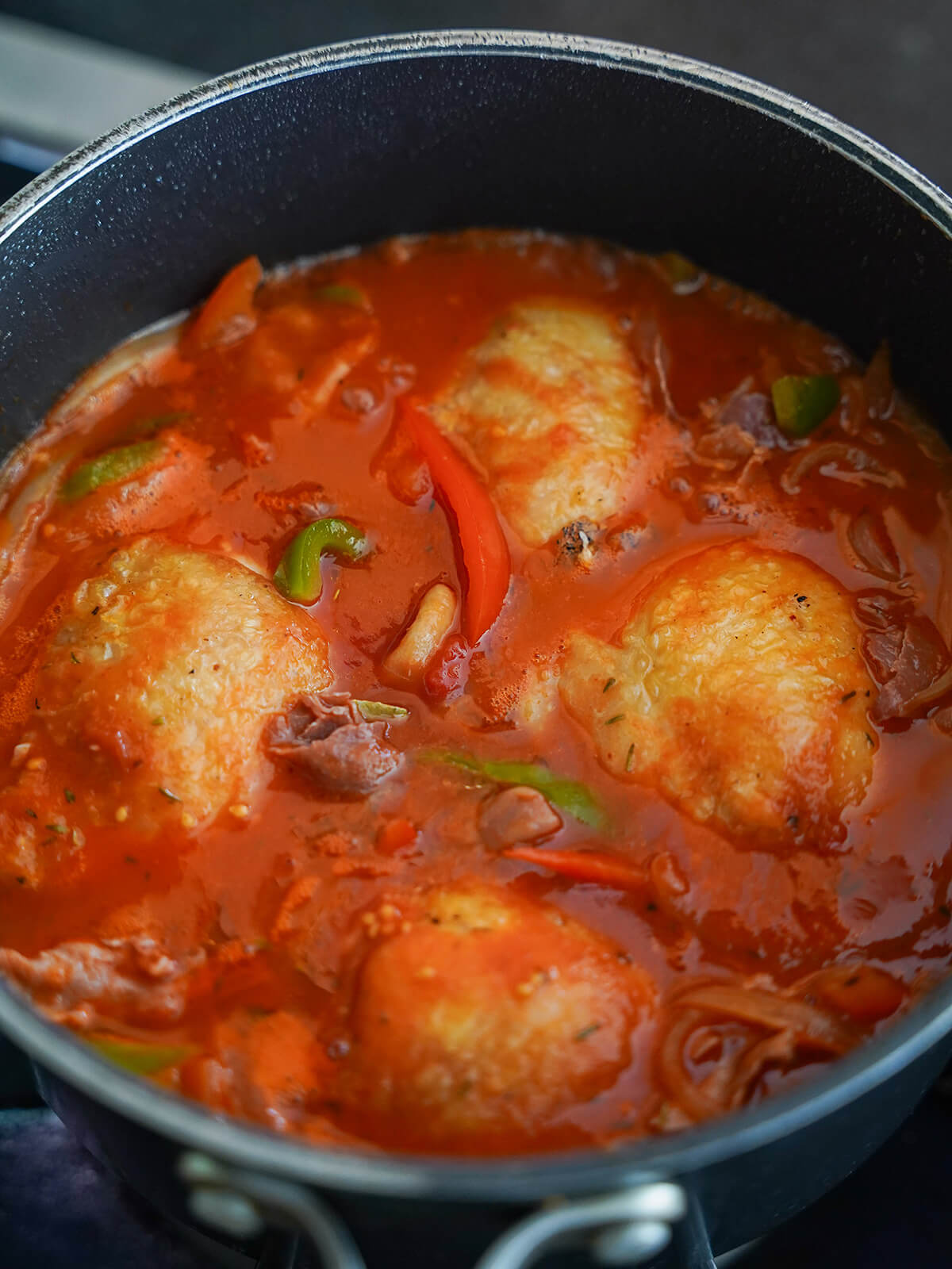 pieces of chicken in under tomato and pepper sauce before cooking down.