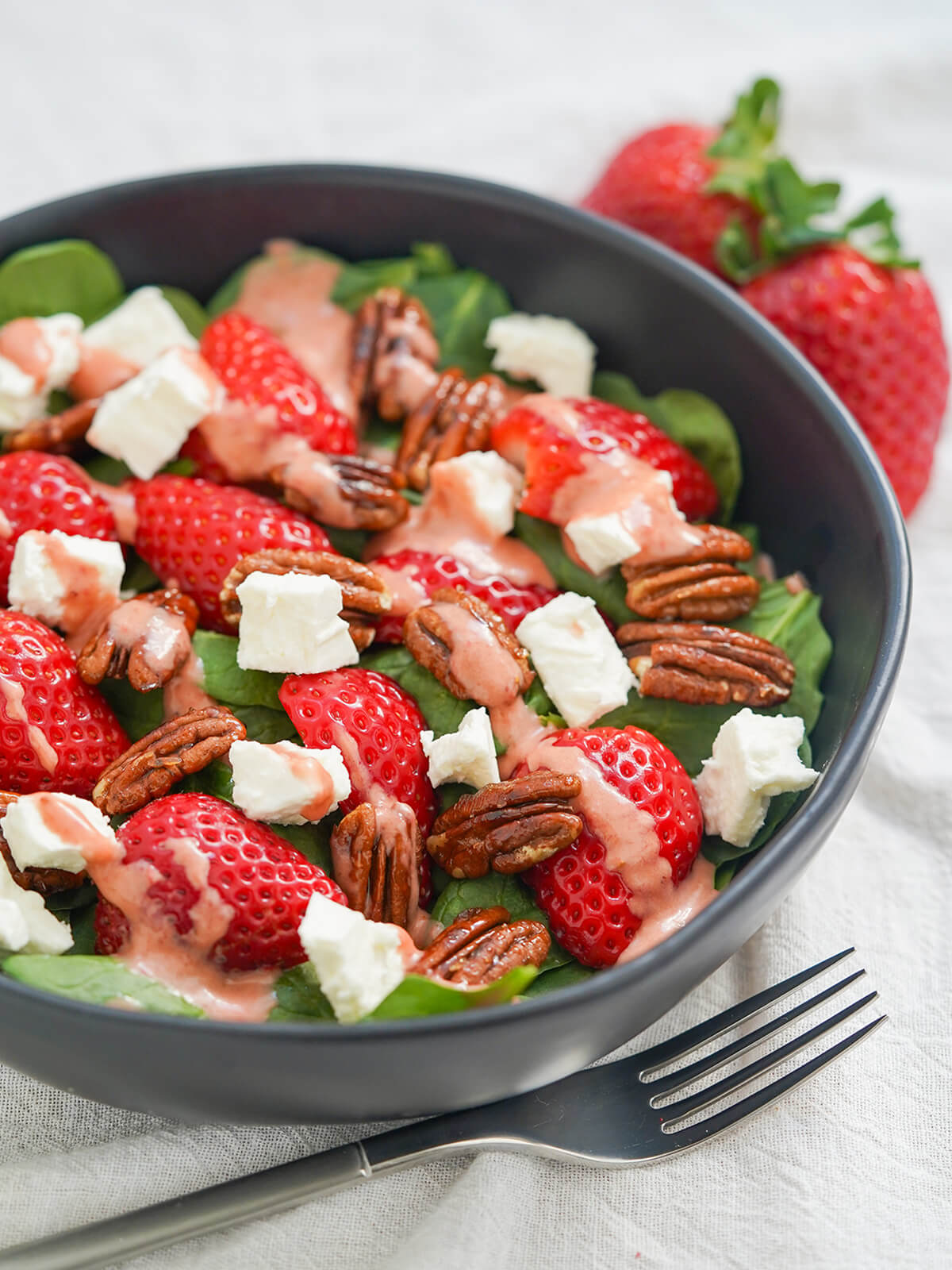 side view of bowl of spinach and strawberry salad with fork in front below bowl.