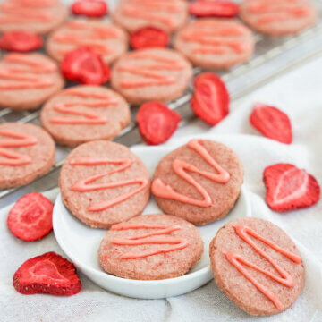 small plate with some strawberry shortbread cookies on it with one resting on side, more behind and pieces of dried strawberry around.