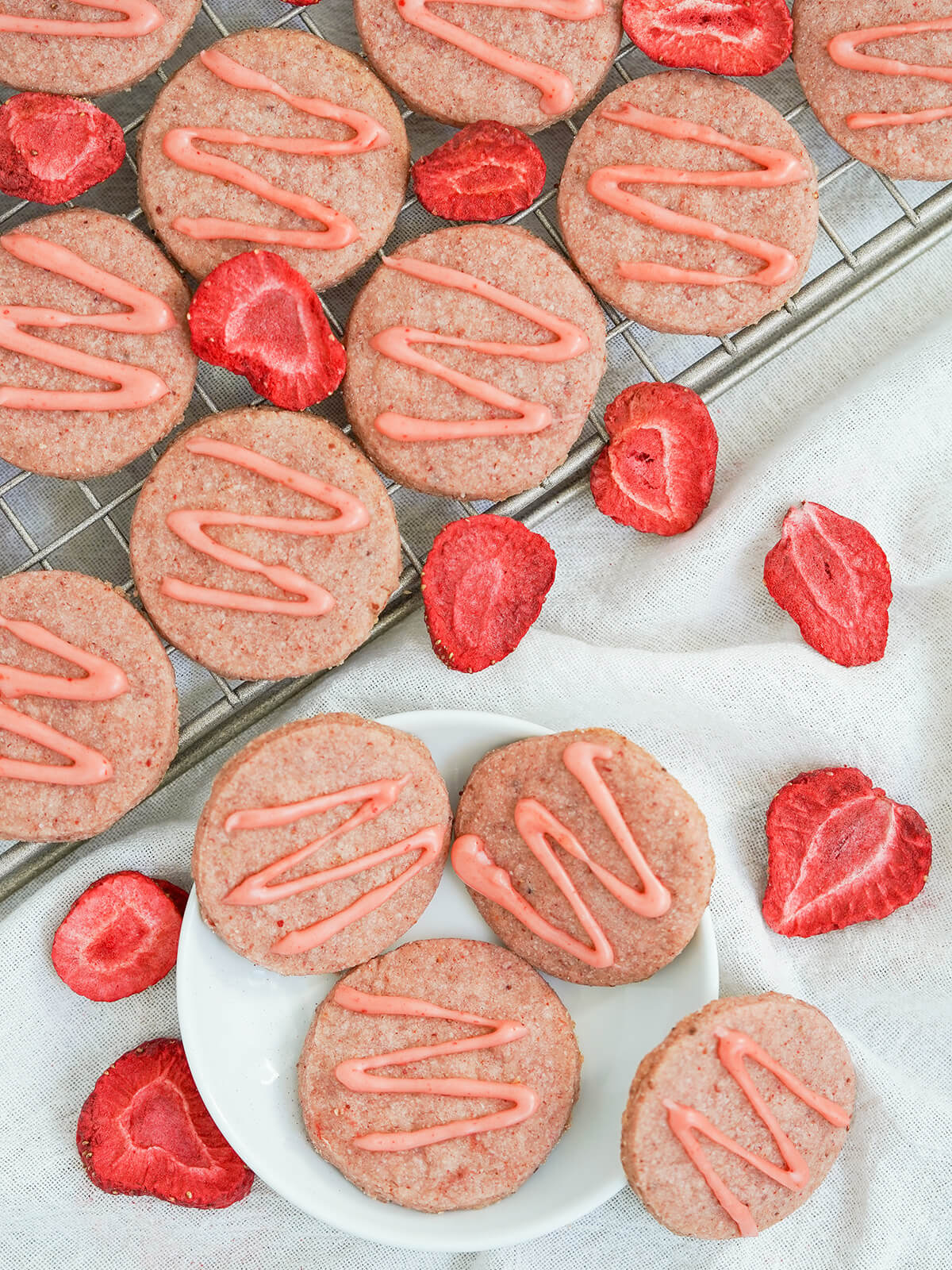 overhead view of strawberry shortbread cookies on rack and plate with freeze dried strawberries around.