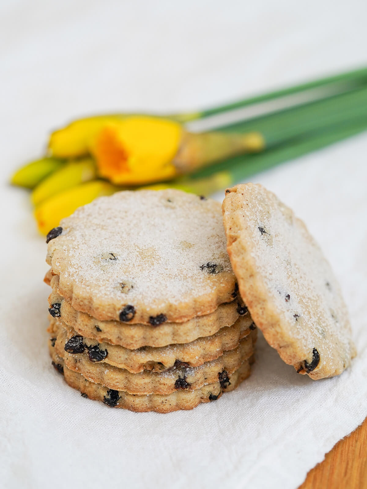 stack of Easter biscuits with one resting on side with bunch of daffodils blurred in background.