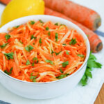 side view of bowl of German carrot apple salad with part view of carrots and lemon behind.