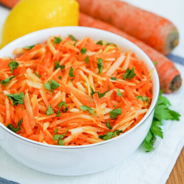 side view of bowl of German carrot apple salad with part view of carrots and lemon behind.