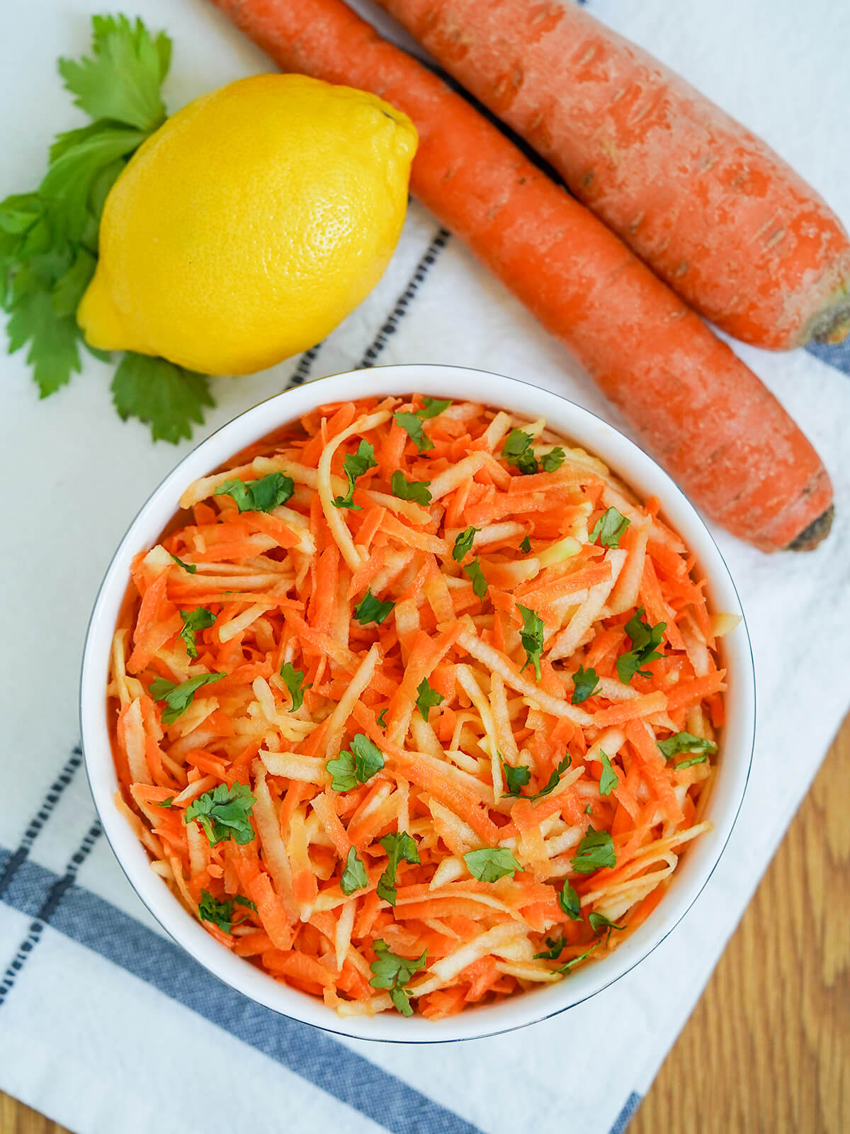 overhead view of a bowl of German carrot apple salad with carrots, lemon and parsley sprig above bowl.