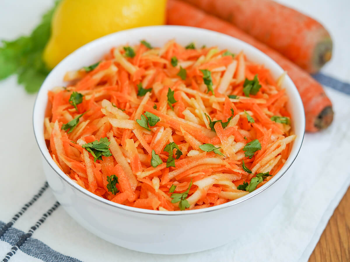 bowl of German carrot apple salad with small pieces of parsley on top to garnish.