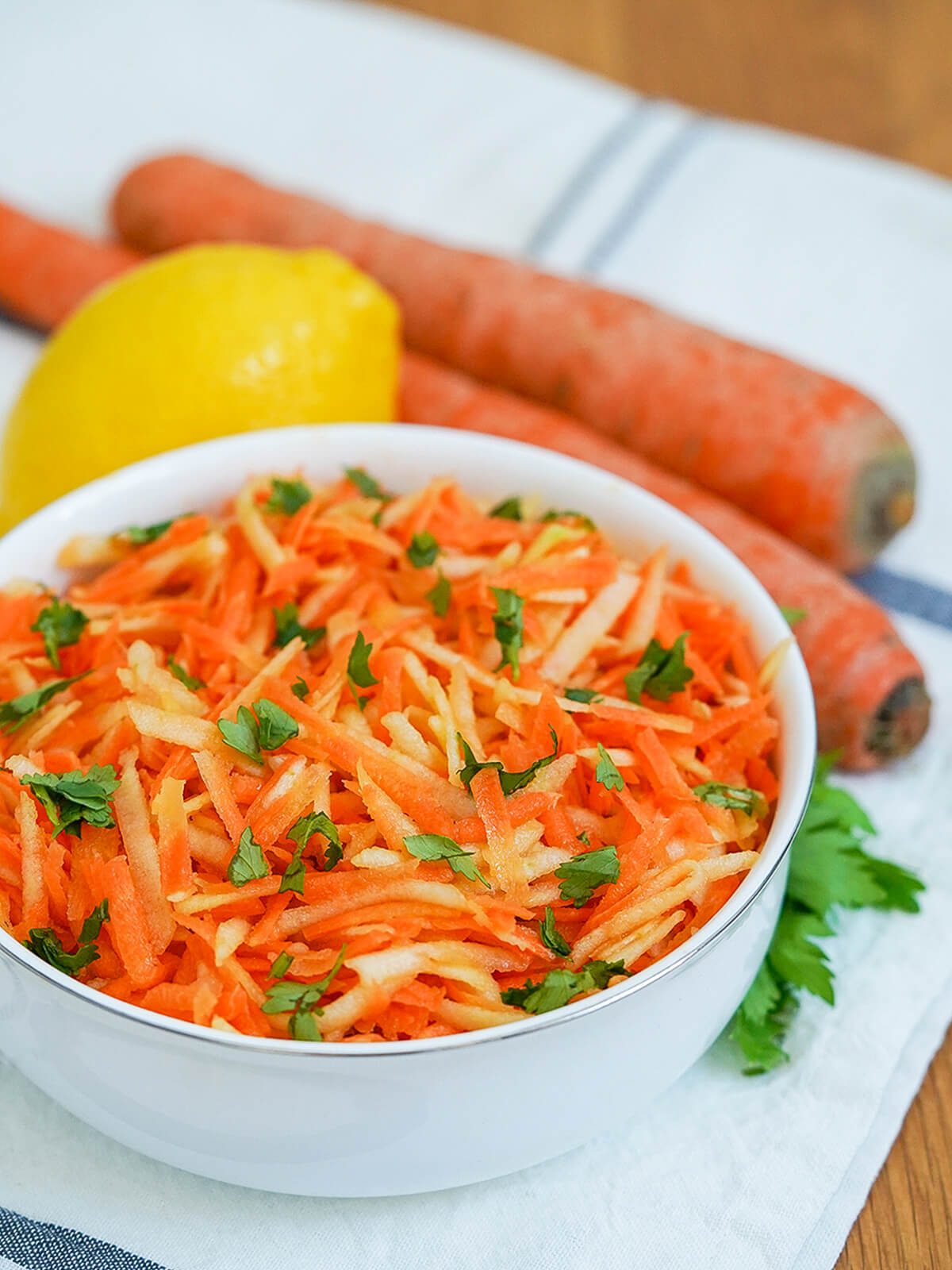 side view of bowl of German carrot apple salad with carrots and lemon behind bowl.