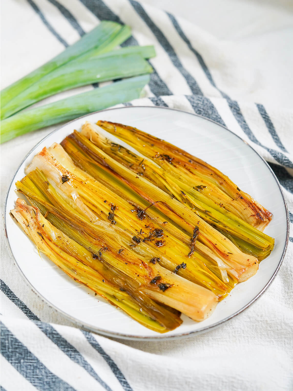 plate of braised leeks with tops of uncooked leeks in background.