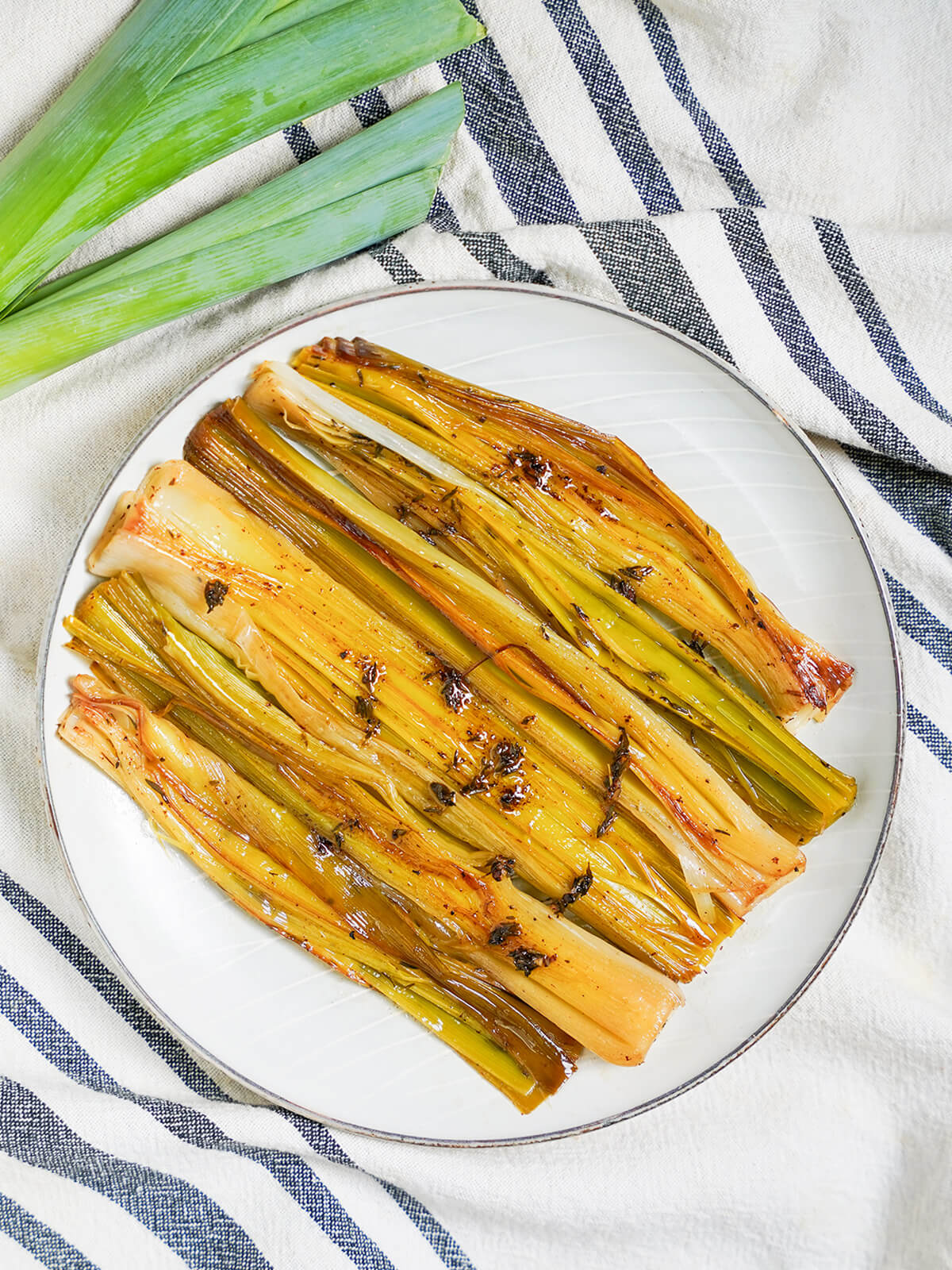 overhead view of a plate of braised leeks with leek tops in top left corner.