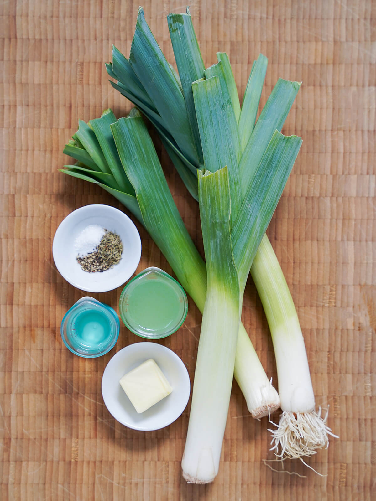leeks, butter and measures with wine and stock on wooden board, plus small dish with salt, pepper and thyme.