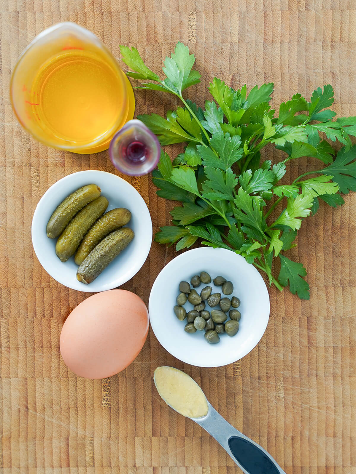bunch of parsley, dishes with cornichons and capers, egg, spoon of mustard, measures with oil and vinegar.