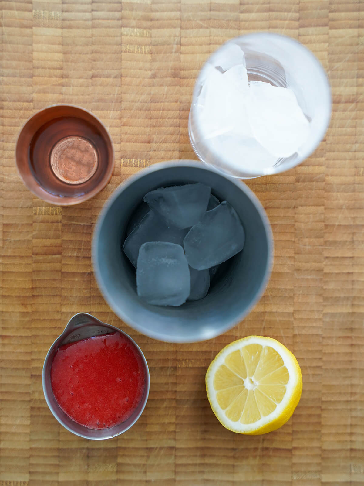 cocktail shaker with ice with measure of strawberry puree, part lemon and measure with gin around it.