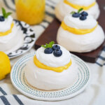plate with a mini lemon pavlova on it topped with blueberries with bore in part view behind.