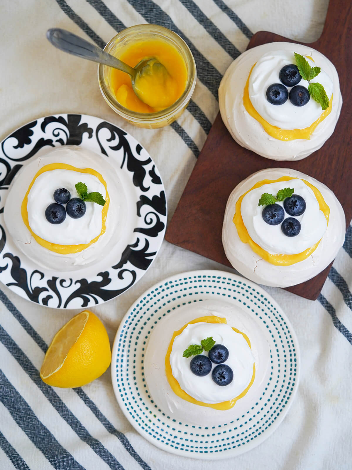 overhead view of four mini lemon pavlova on plates and board as well as jar of lemon curd and cut lemon.