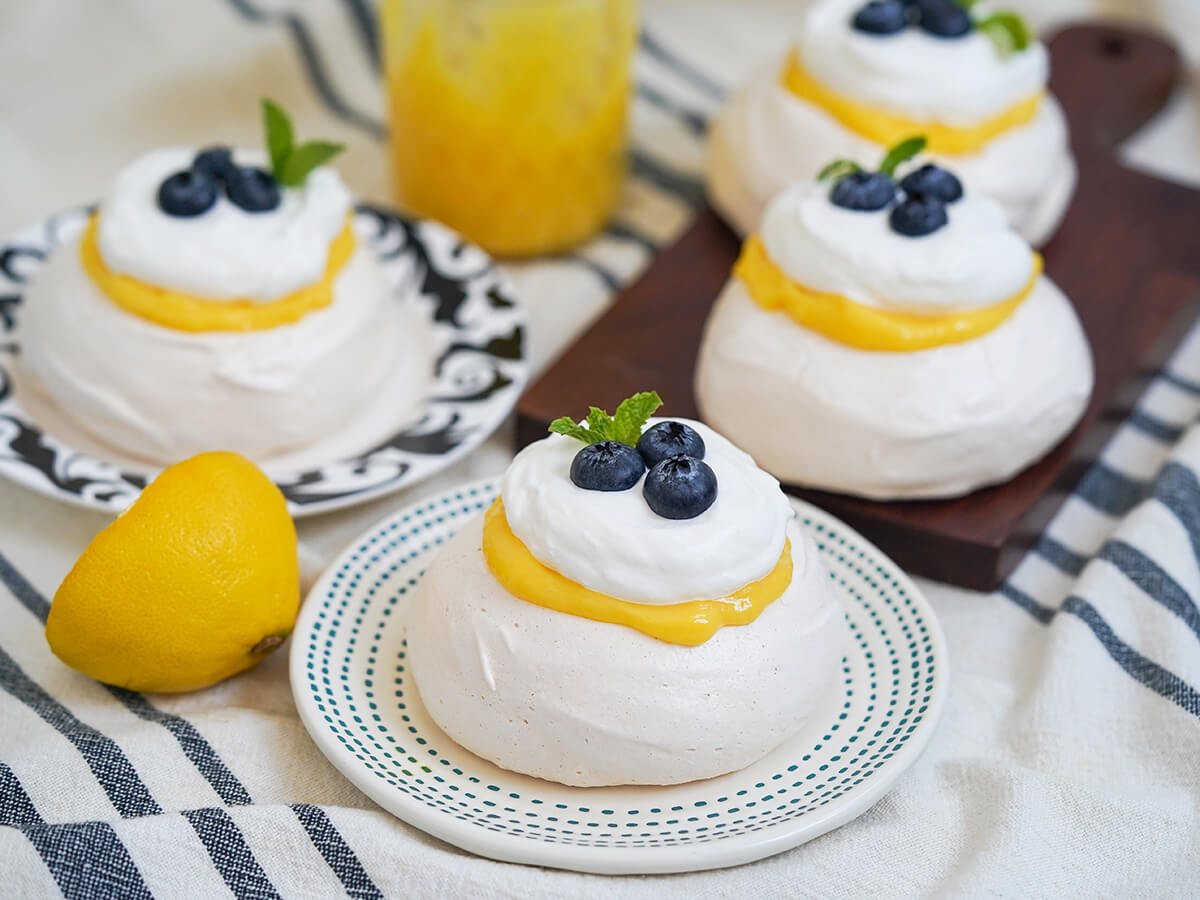 four mini lemon pavlova with two on plates and other on wooden board behind.