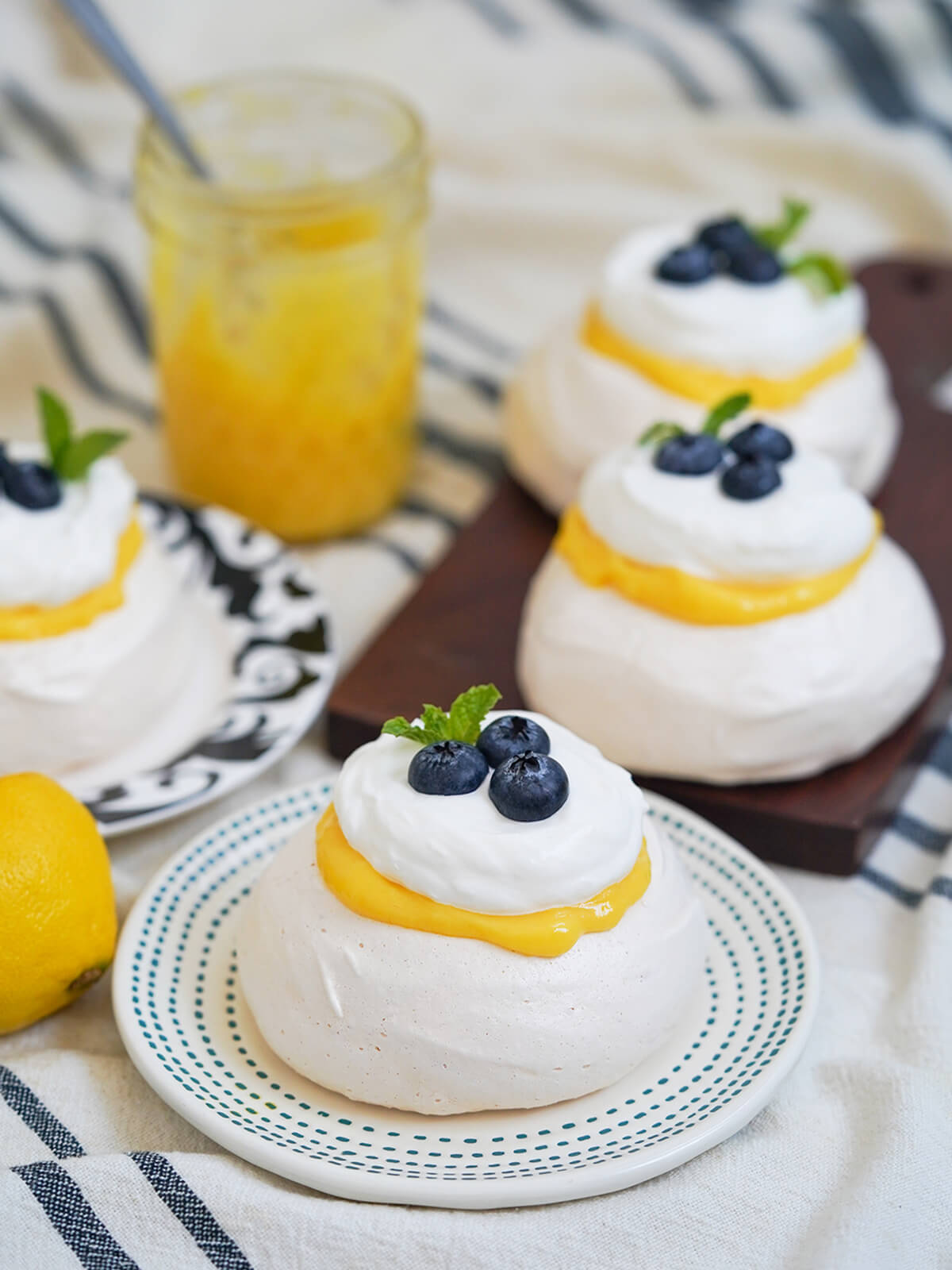 plate with a mini lemon pavlova on it with two more on board behind and jar of lemon curd in background.