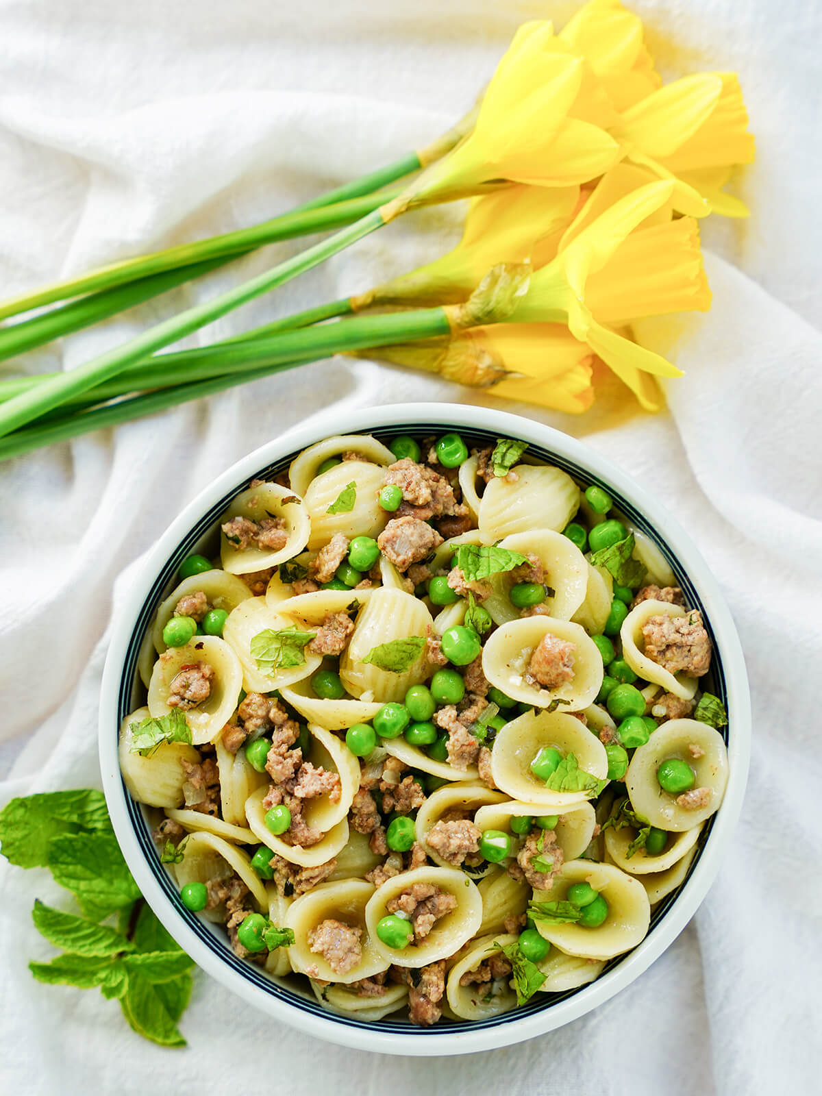 overhead view of a bowl of pea and lamb pasta with daffodils above bowl.