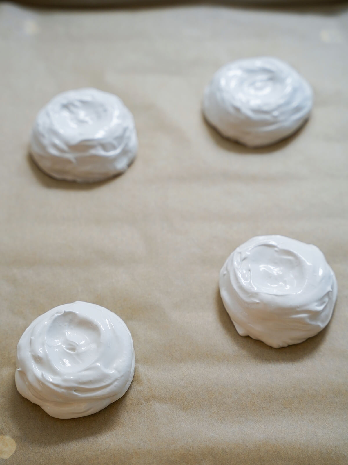 four mounds of pavlova mixture on parchment before baking.