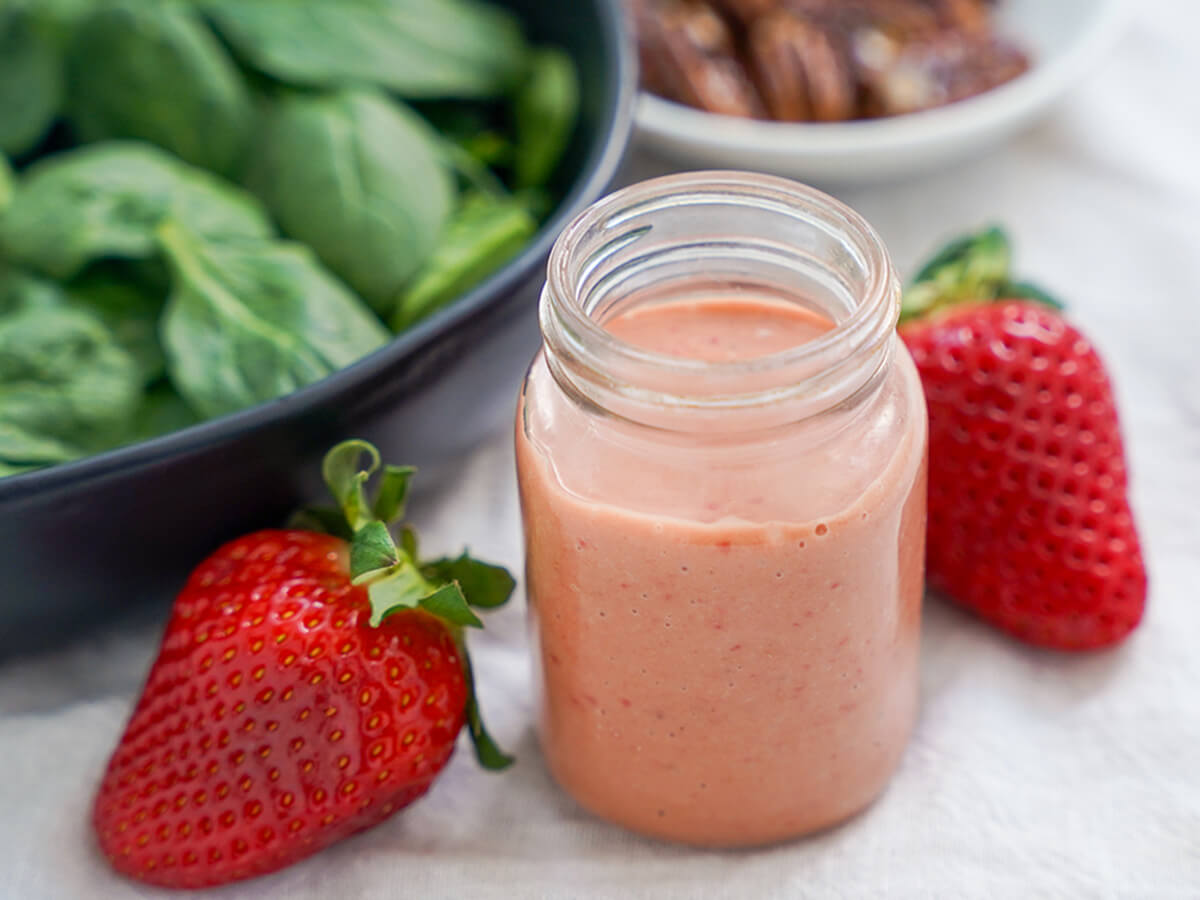 strawberry balsamic vinaigrette with strawberry either side and greens in dish behind.