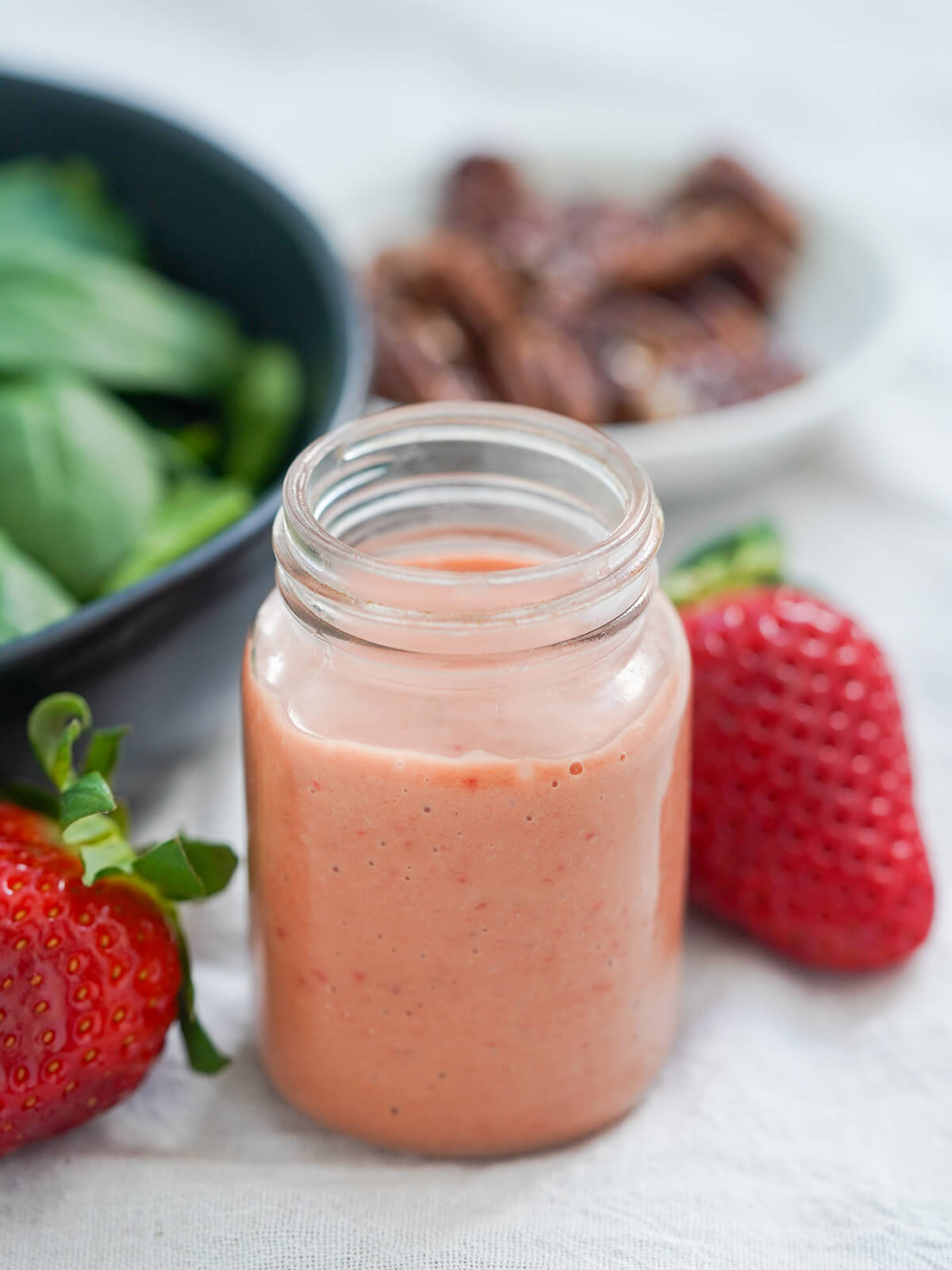 jar of strawberry balsamic vinaigrette with strawberry behind jar and blurred bowl of greens and nuts behind.
