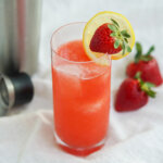 glass of strawberry collins garnished with slice of lemon and a strawberry.