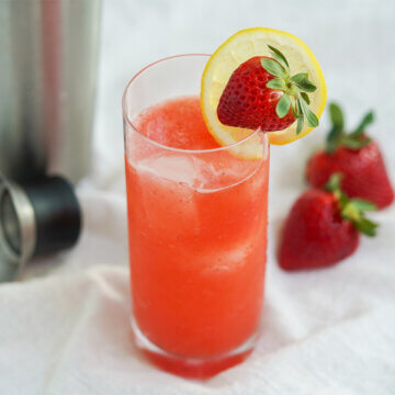 glass of strawberry collins garnished with slice of lemon and a strawberry.