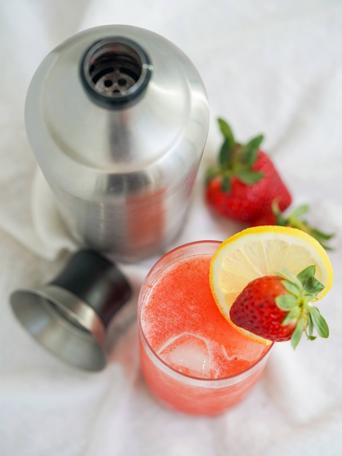 looking from overhead into glass of strawberry collins and cocktail shaker.