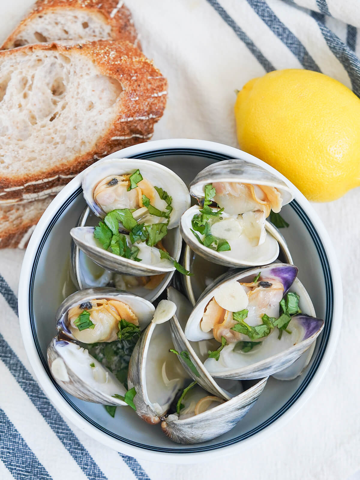 overhead view of bowl of Portuguese clams with lemon and slices of bread above bowl.