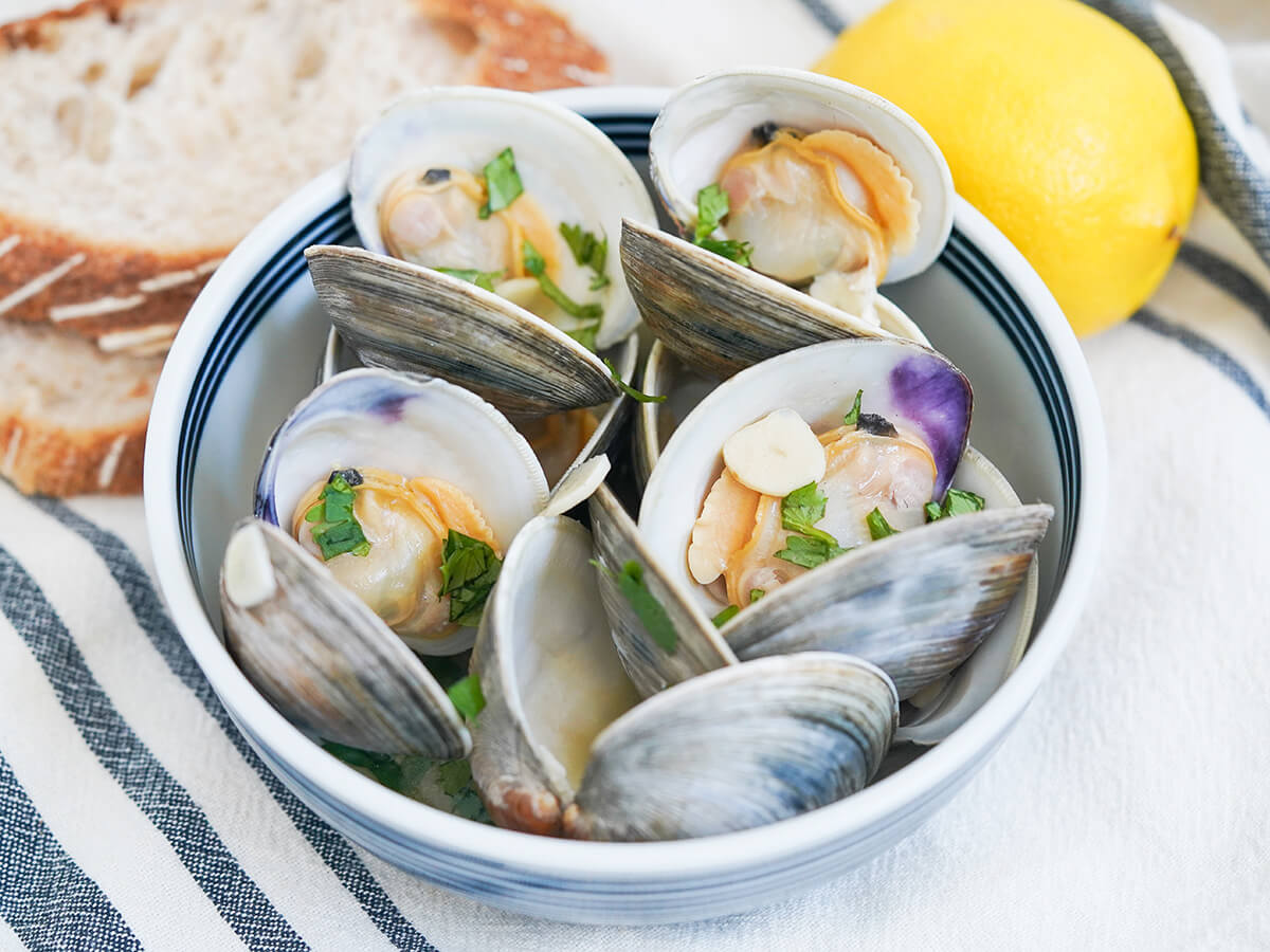 side view of bowl of Portuguese clams showing pieces of cilantro and garlic on top.