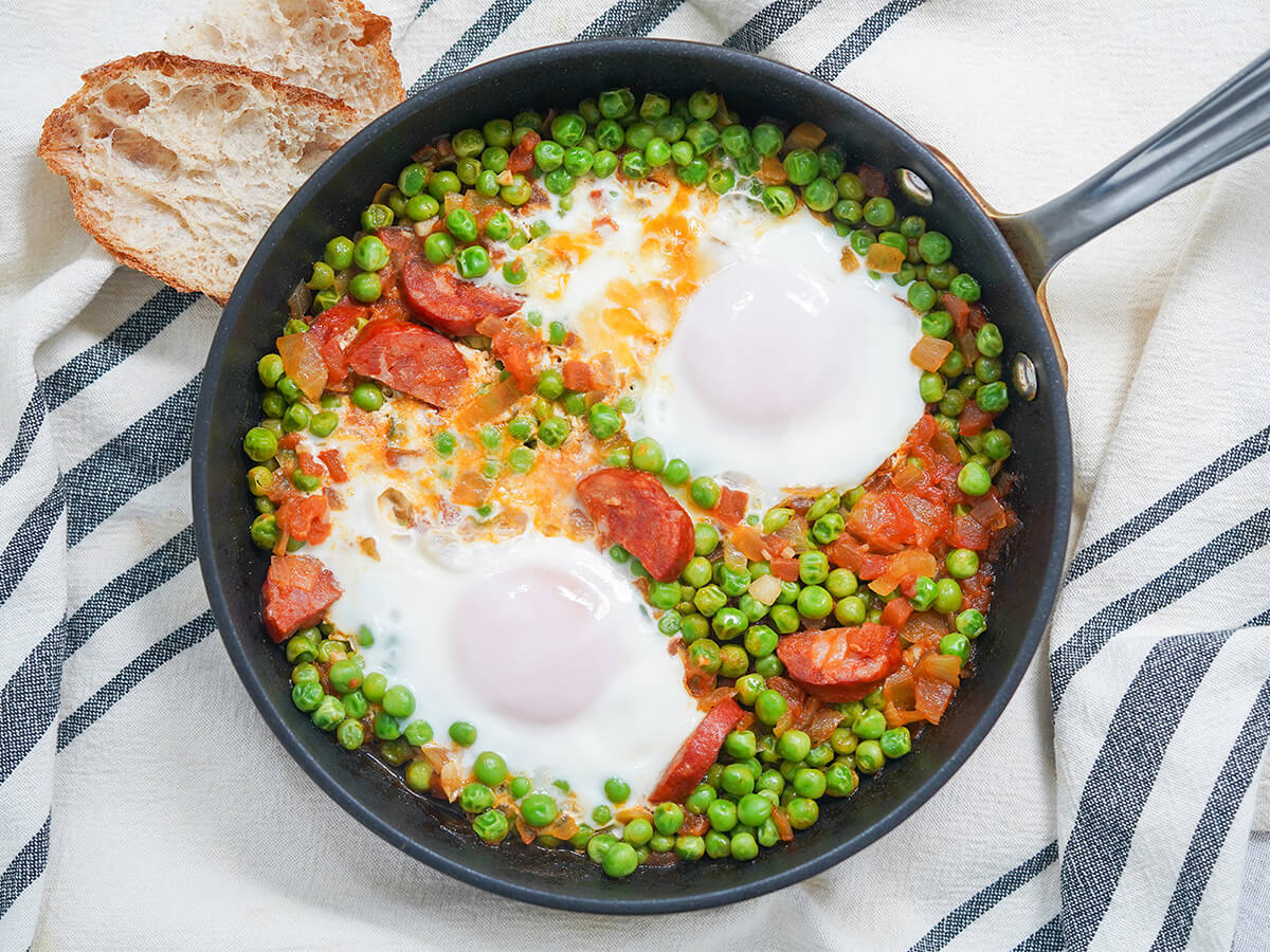 overhead view of skillet of Portuguese peas and eggs with piece of bread above skillet.