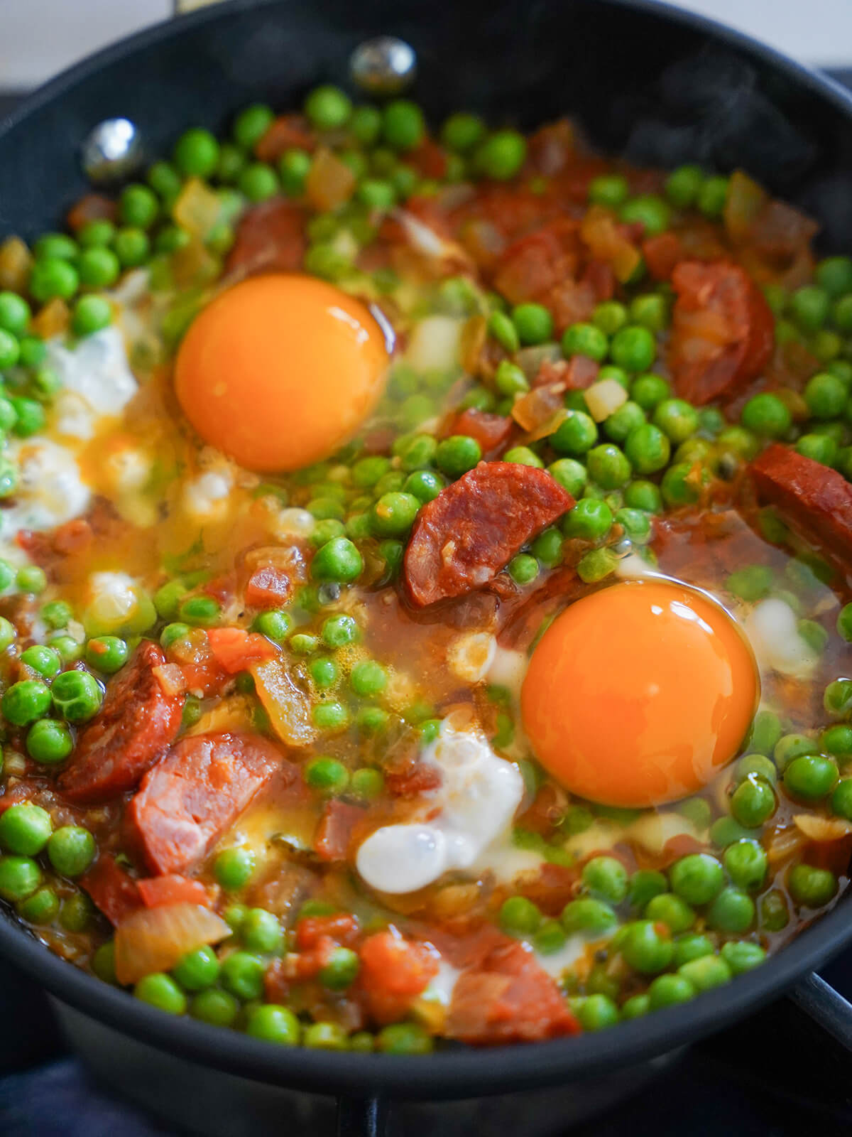 adding eggs into pea, chourico and tomato mixture.