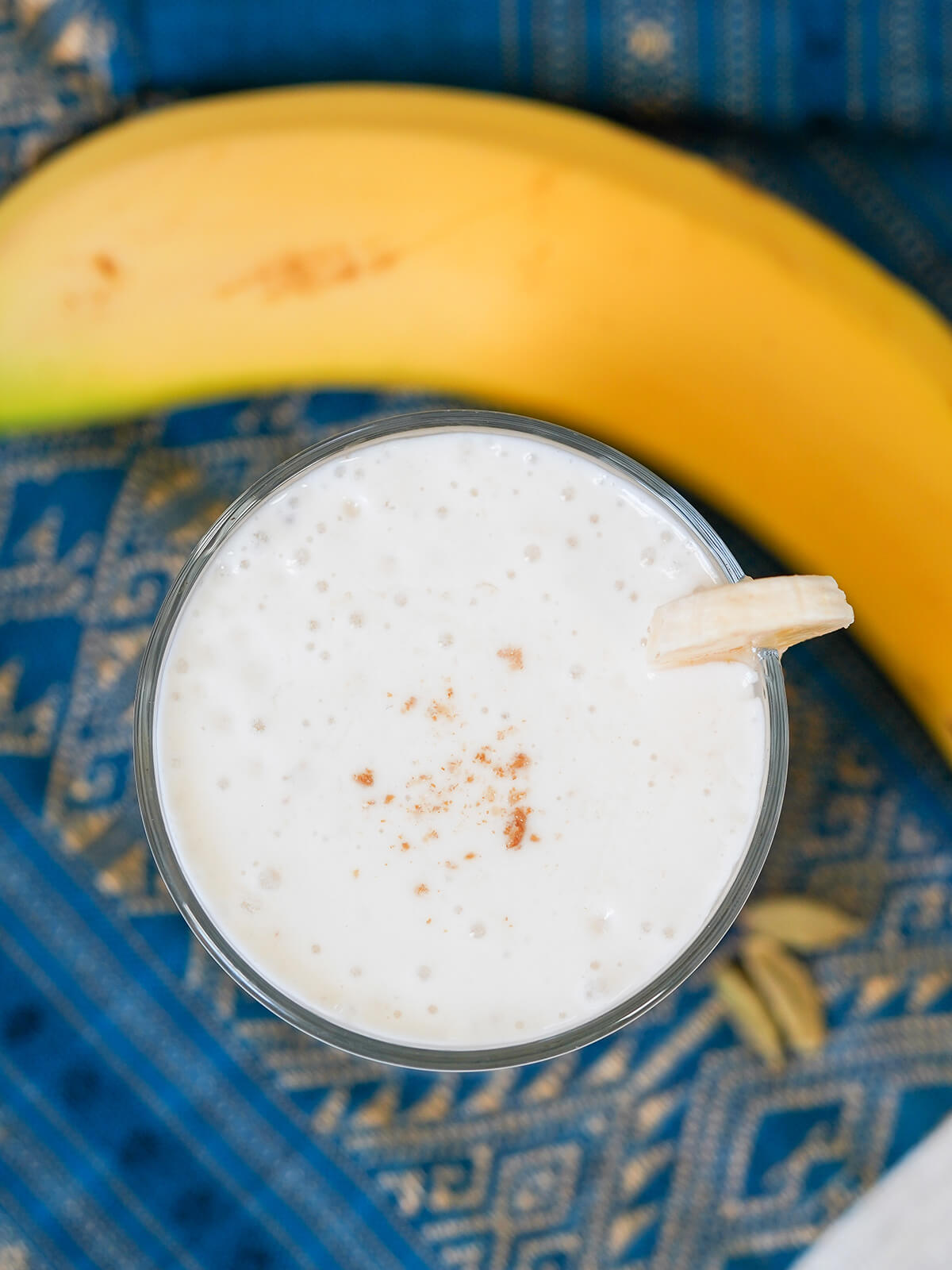 overhead view of glass of banana lassi with banana above glass.